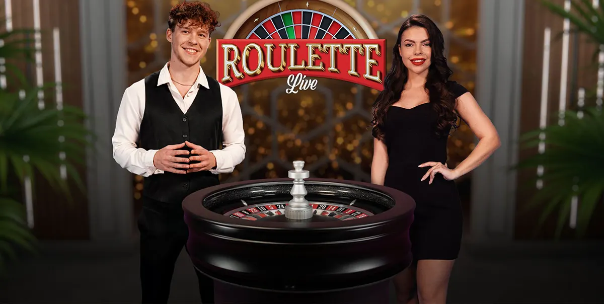 Two live roulette hosts—a man in a black vest and a woman in a black dress—stand beside a roulette wheel under a “Roulette Live” sign in a glossy casino-style studio.